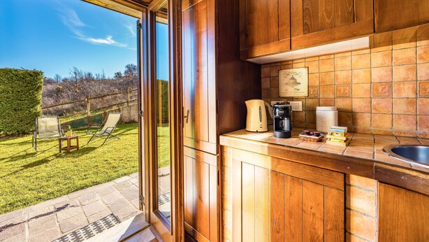 A kitchen with wooden cabinets, a tiled backsplash, and a view of a grassy yard through an open door. - Rifugio Marley in Pescocostanzo (Pescocostanzo)