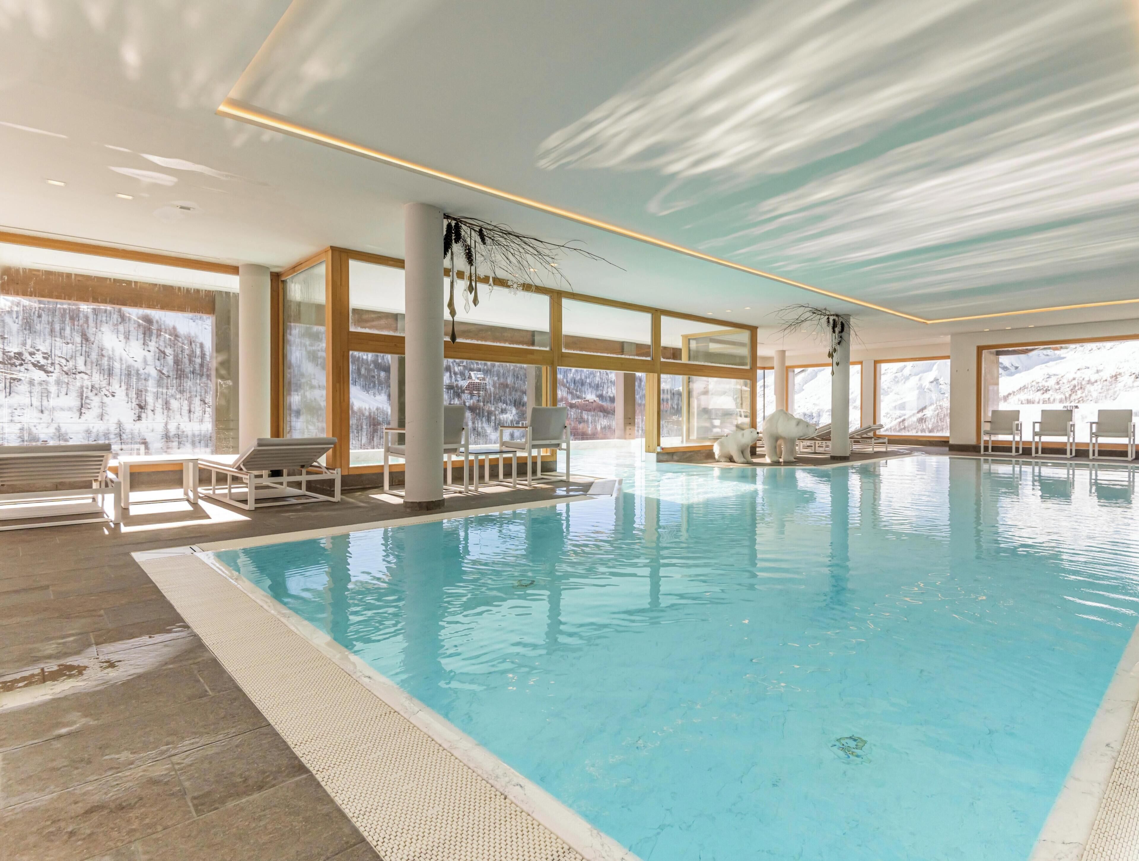 An indoor swimming pool with clear views of snowy mountains through large windows.