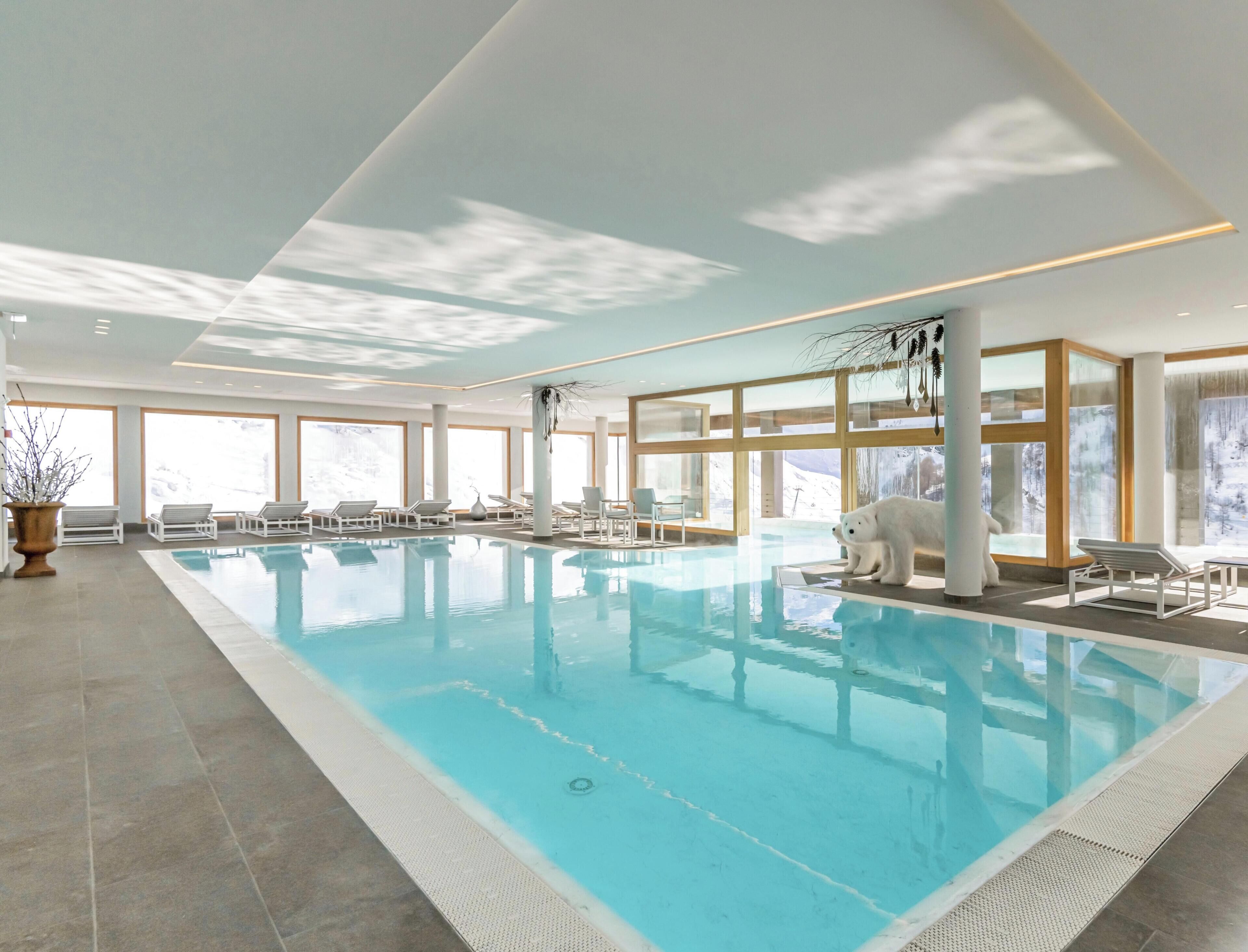 An indoor swimming pool with clear views of snowy mountains through large windows.
