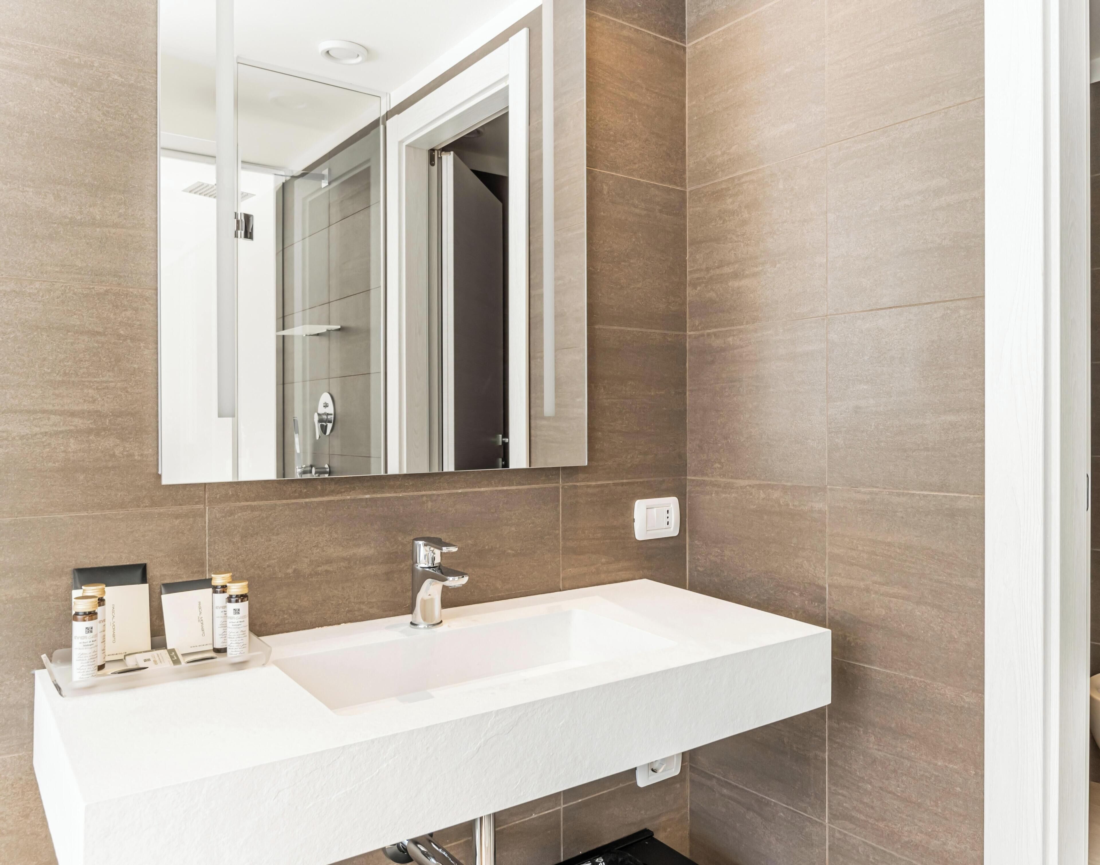 A modern bathroom with a white sink, a large mirror, and brown tiled walls.