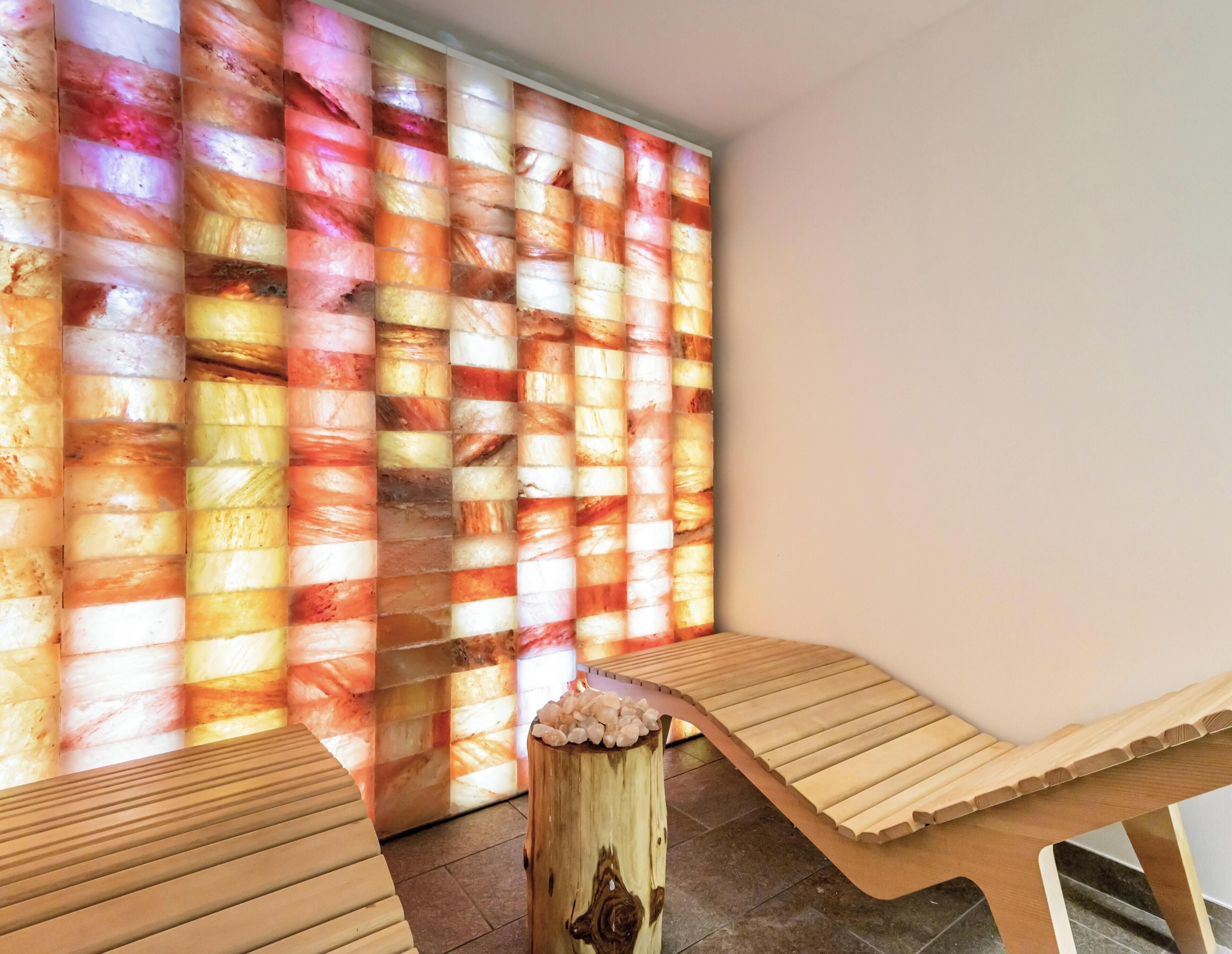 Quarto com divisória de vidro colorido e dois bancos de madeira.