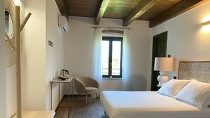 A bedroom with a wooden bed, a desk with a chair, a window with curtains, and a wall-mounted lamp. - Cascina 1909 (Priocca)