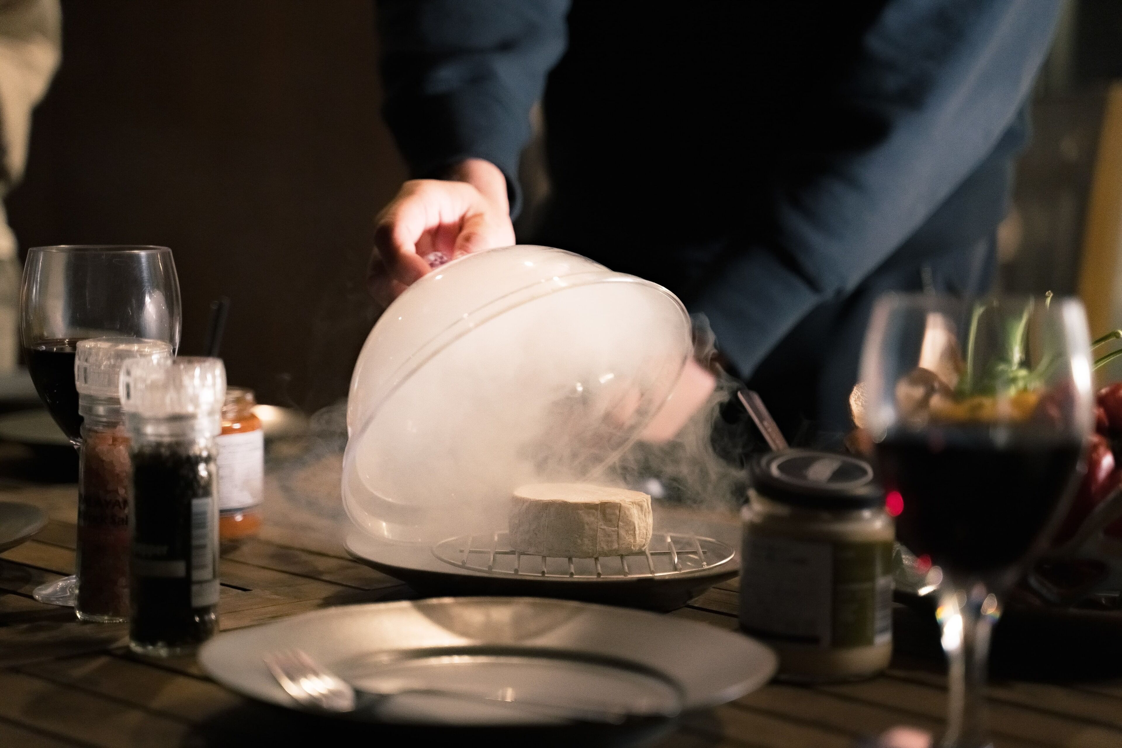 A cheese dish on a table with condiments and a wine glass.