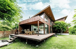 Une maison moderne dotée d’une terrasse en bois, de grandes fenêtres et d’un vaste espace extérieur.