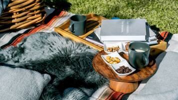 A picnic setup with a blanket, a book, a mug, and snacks on a wooden tray.