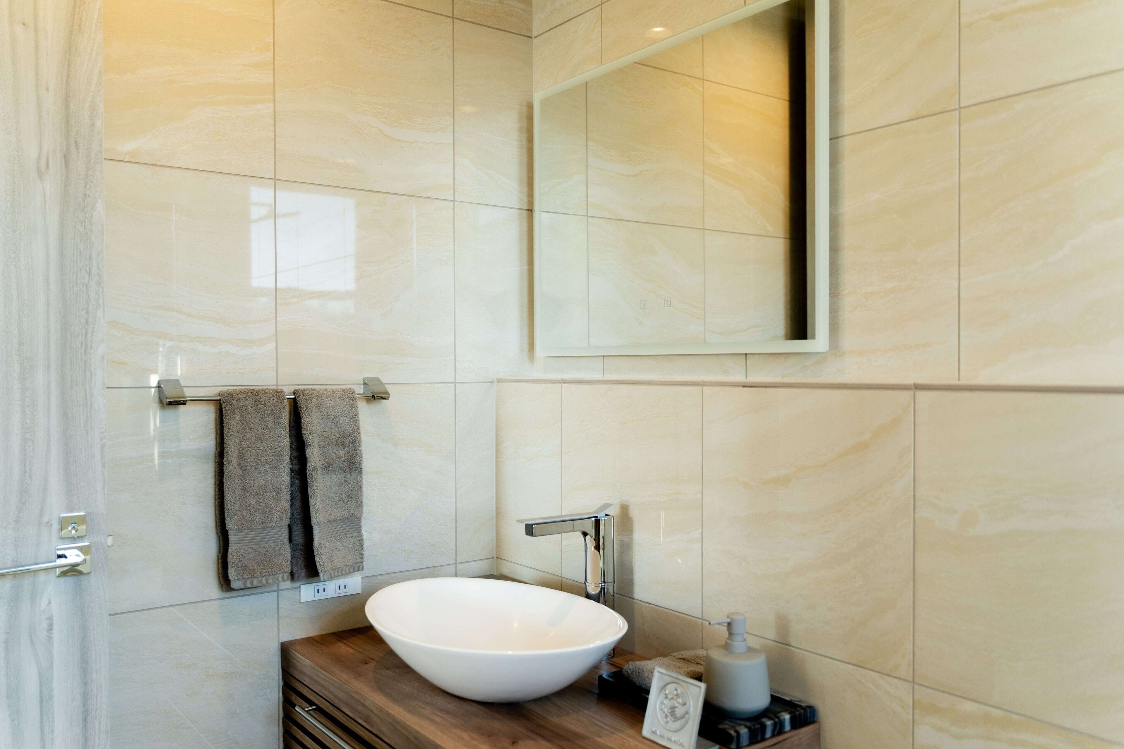 A modern bathroom with a large mirror, a white vessel sink, and a wooden vanity.
