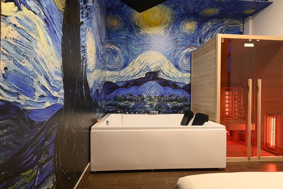 A modern bathroom with a large bathtub, a wall mural, and a glass door leading to a shower area.