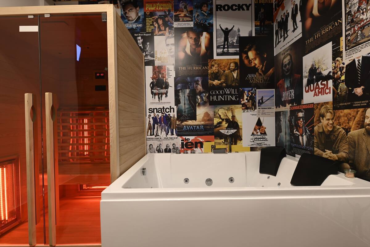 A room with a large wall of movie posters, a white bathtub, and a wooden door.