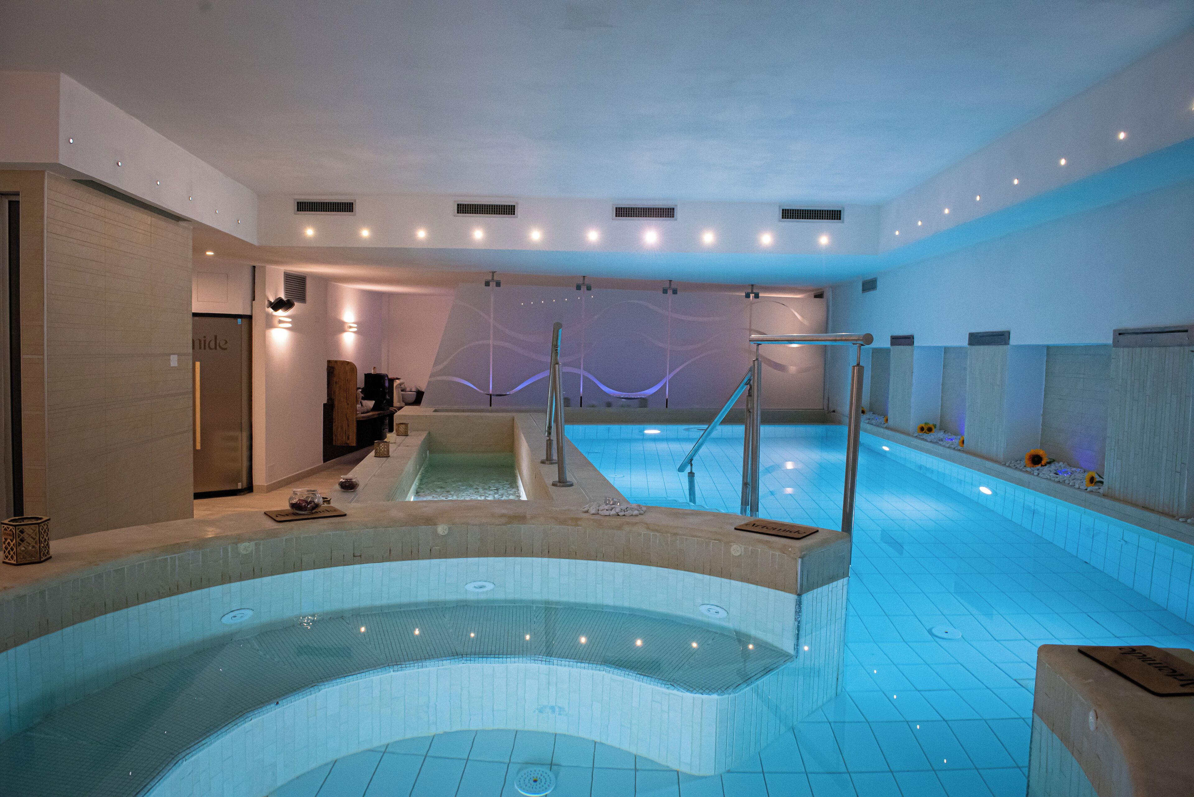 Piscina interior moderna com área de hidromassagem, sala de trocas e balcão de recepção.