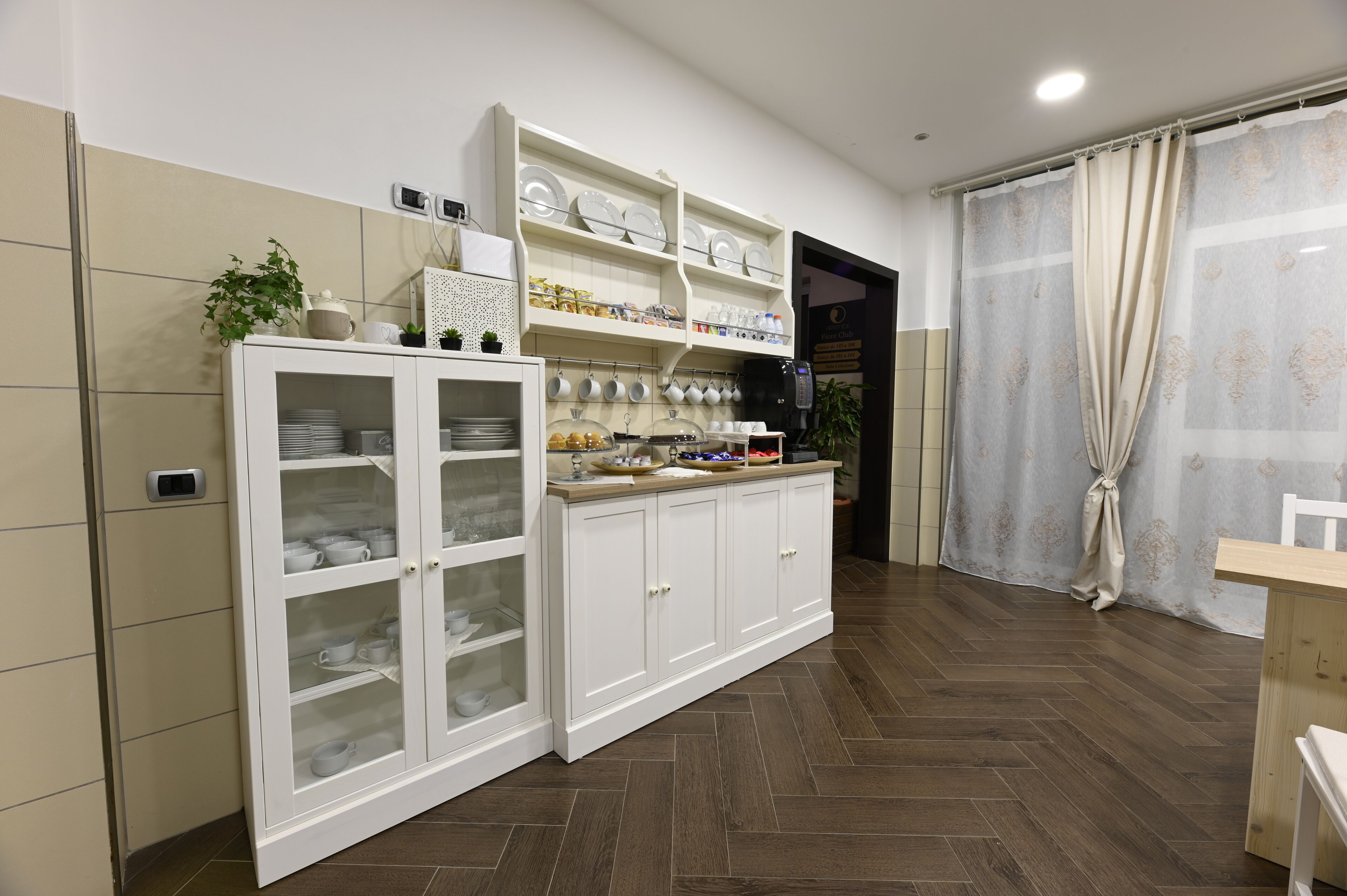 Una cocina con armarios blancos, suelo de madera en espiga y un comedor con mesa de madera.