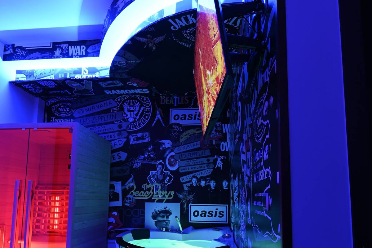 A room with a curved wall decorated with band logos, a bed, and a desk with a chair.