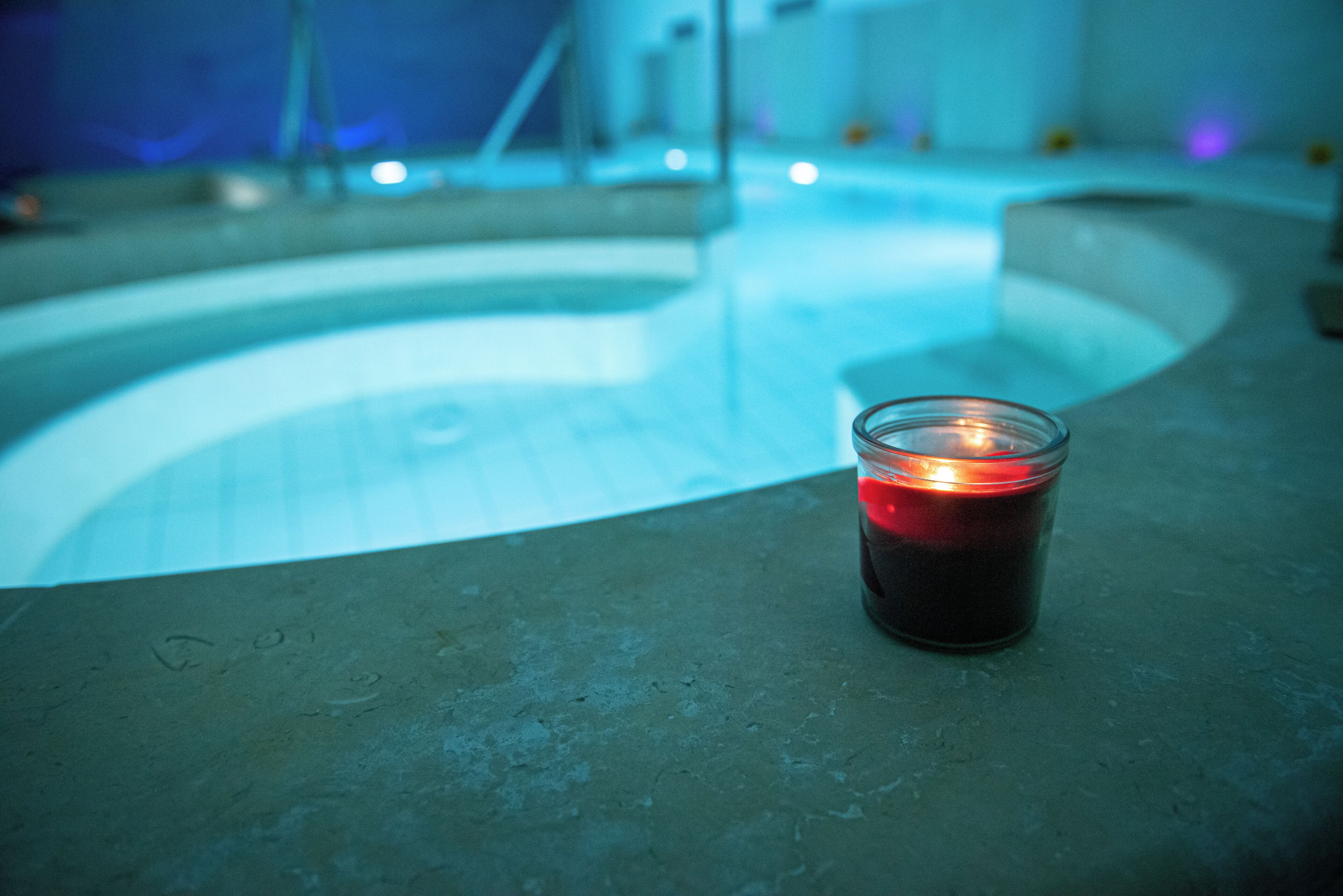 A candle on a concrete surface near a pool with a curved edge.