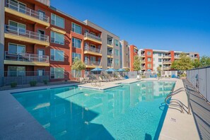 A modern apartment building with a swimming pool, outdoor seating, and a clear blue sky.