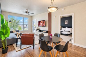 A modern living room with a sofa, coffee table, and chairs, a dining area with a table and chairs, a TV mounted on the wall, and a bedroom with a bed and a nightstand. - Group-Friendly Apt with Pool,Gym,Parking,WD,Balcon (Tempe)