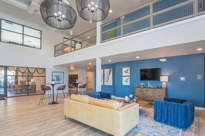 A spacious lobby with a high ceiling, a seating area with a sofa and chairs, a bar area, and artwork on the walls.