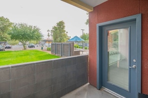 A balcony with a view of a parking lot, a grassy area, and a building with a blue door.