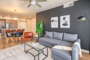 A modern living room with a grey sofa, a coffee table, and a dining area with chairs and a table. - Family-Friendly Apt | Pool,Gym,W/D,Parking,Balcony (Tempe)