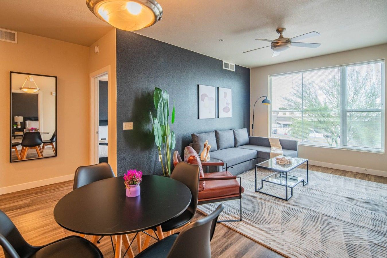 Un salon moderne comprenant un coin repas, un canapé gris, une table basse et une grande fenêtre.