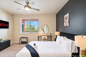 A hotel room with a bed, a desk, a chair, a ceiling fan, a TV, and a window with blinds. - Family-Friendly Apt | Pool,Gym,W/D,Parking,Balcony (Tempe)