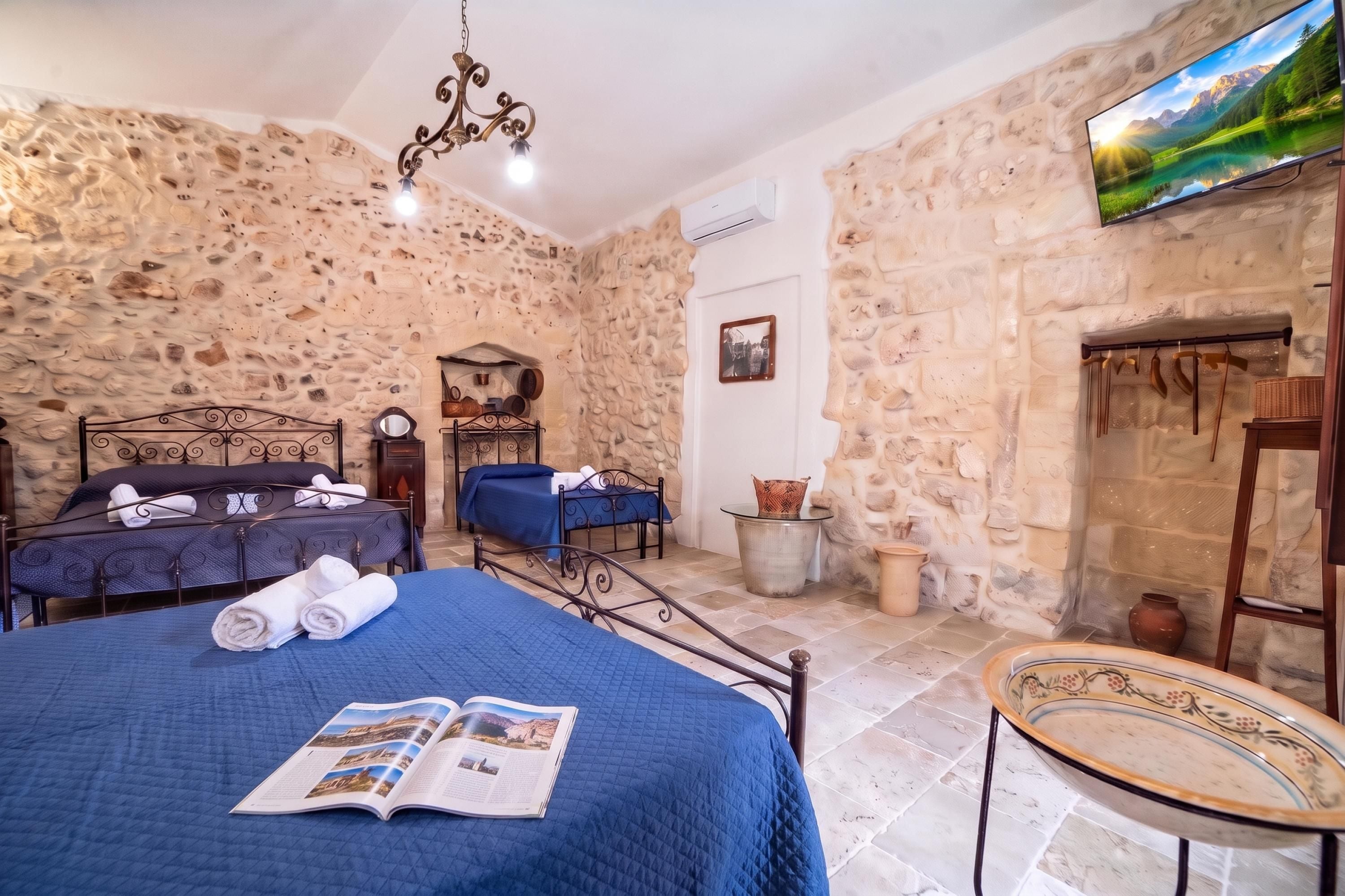 A bedroom with stone walls, two beds, a chandelier, and a fireplace.