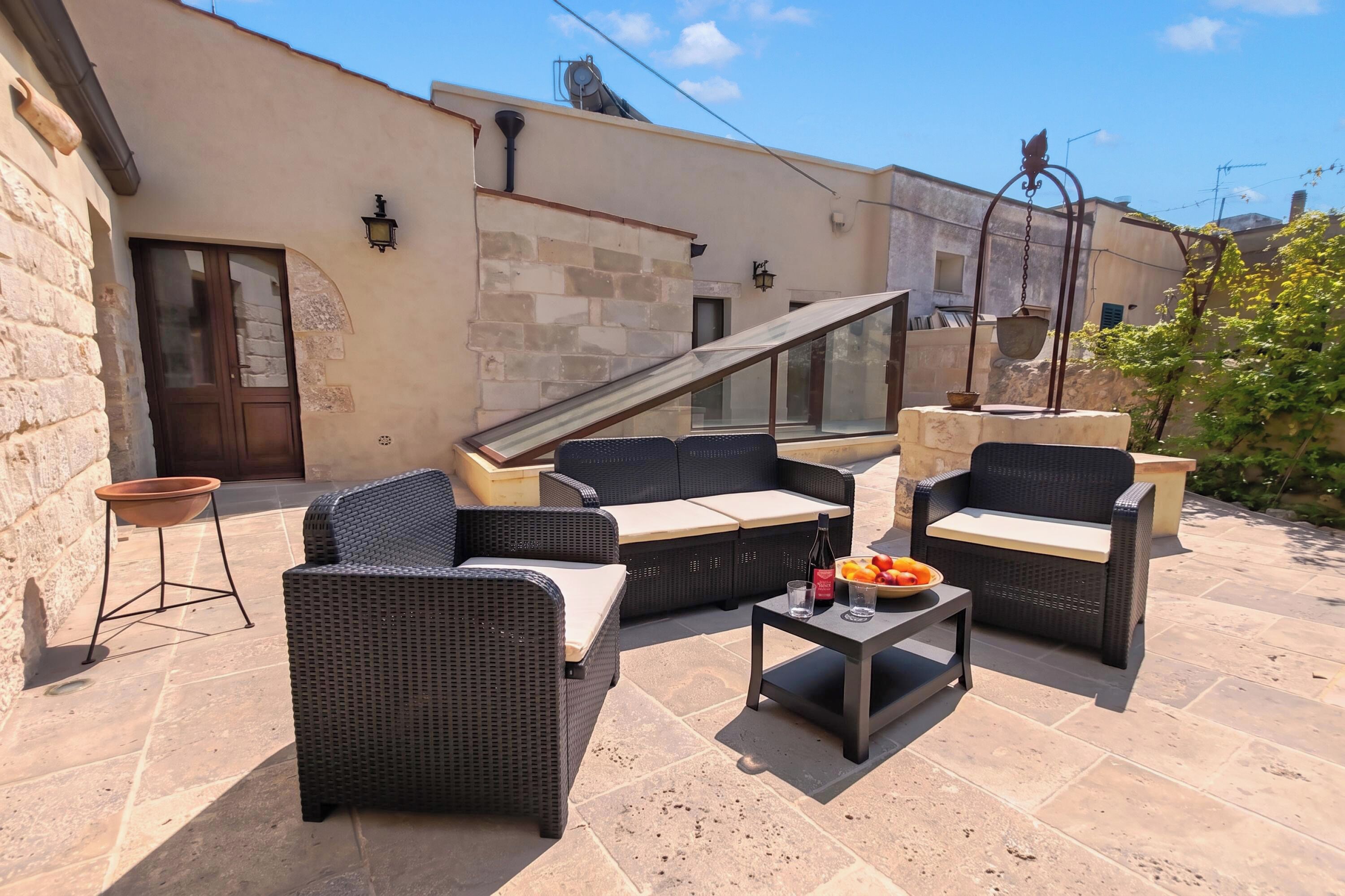 An outdoor seating area with wicker furniture and a table with fruit and a bottle.