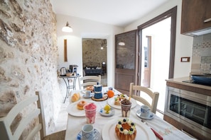 A dining area with a stone wall, a table set with plates, cups, and a variety of food items. There is a kitchen area with a stove and oven visible. - Corte San Giorgio Apartments with airco (Martano)