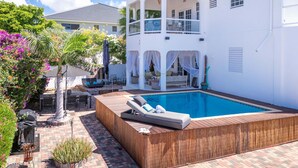 Ein Poolbereich mit Holzterrasse, Liegestühlen und einer überdachten Sitzecke mit Blick auf den Pool.