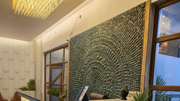 A reception desk with a textured wall and a hanging chandelier. - The Royal Orchid (Aligarh)
