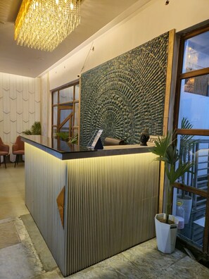 A reception desk with a textured wall and a hanging chandelier. - The Royal Orchid (Aligarh)