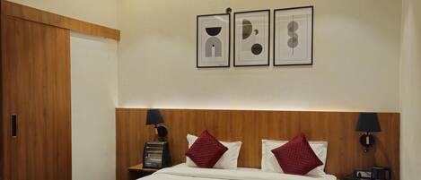 Une chambre d’hôtel avec un lit en bois, une literie rouge et blanche, un ventilateur de plafond et des œuvres d’art encadrées accrochées au mur.