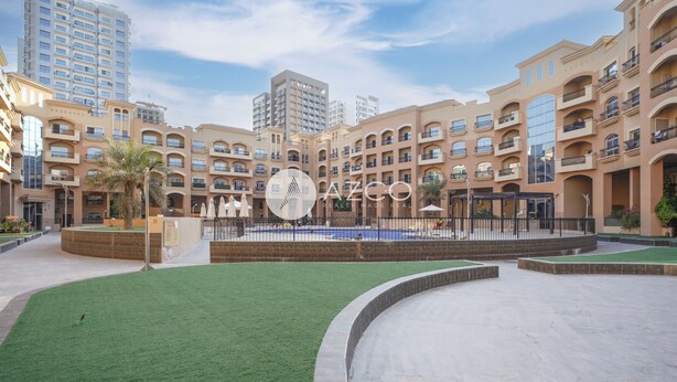 A residential complex with multiple apartment buildings, a central courtyard with artificial grass, and a swimming pool. - Cozy 1 BHK with City View in JVC by AZCO (Dubai)