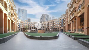 A courtyard with a central circular area, surrounded by multi-story buildings with balconies and a clear sky. - Cozy 1 BHK with City View in JVC by AZCO (Dubai)