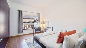 A bedroom with a bed, a window with curtains, a balcony, and a view of buildings. - Cozy 1 BHK with City View in JVC by AZCO (Dubai)