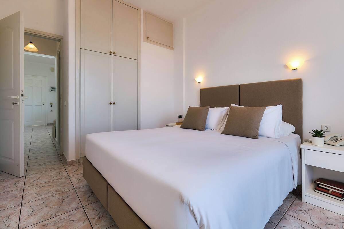 A neatly made bed with white bedding, a bedside table with a lamp, and a wall-mounted light fixture.