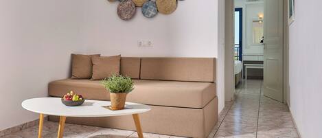 A modern living room with a beige sofa, a round white table with a bowl of fruit and a potted plant, and a wall decorated with circular woven art pieces.