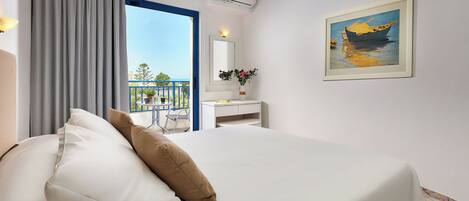 A hotel room with a bed, a desk, a chair, a balcony with a view, and a painting on the wall.
