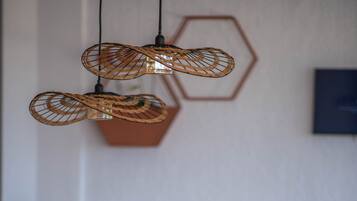 Een eetgedeelte met een houten tafel gedekt voor twee personen, een geweven hanglamp en een bank op de achtergrond.