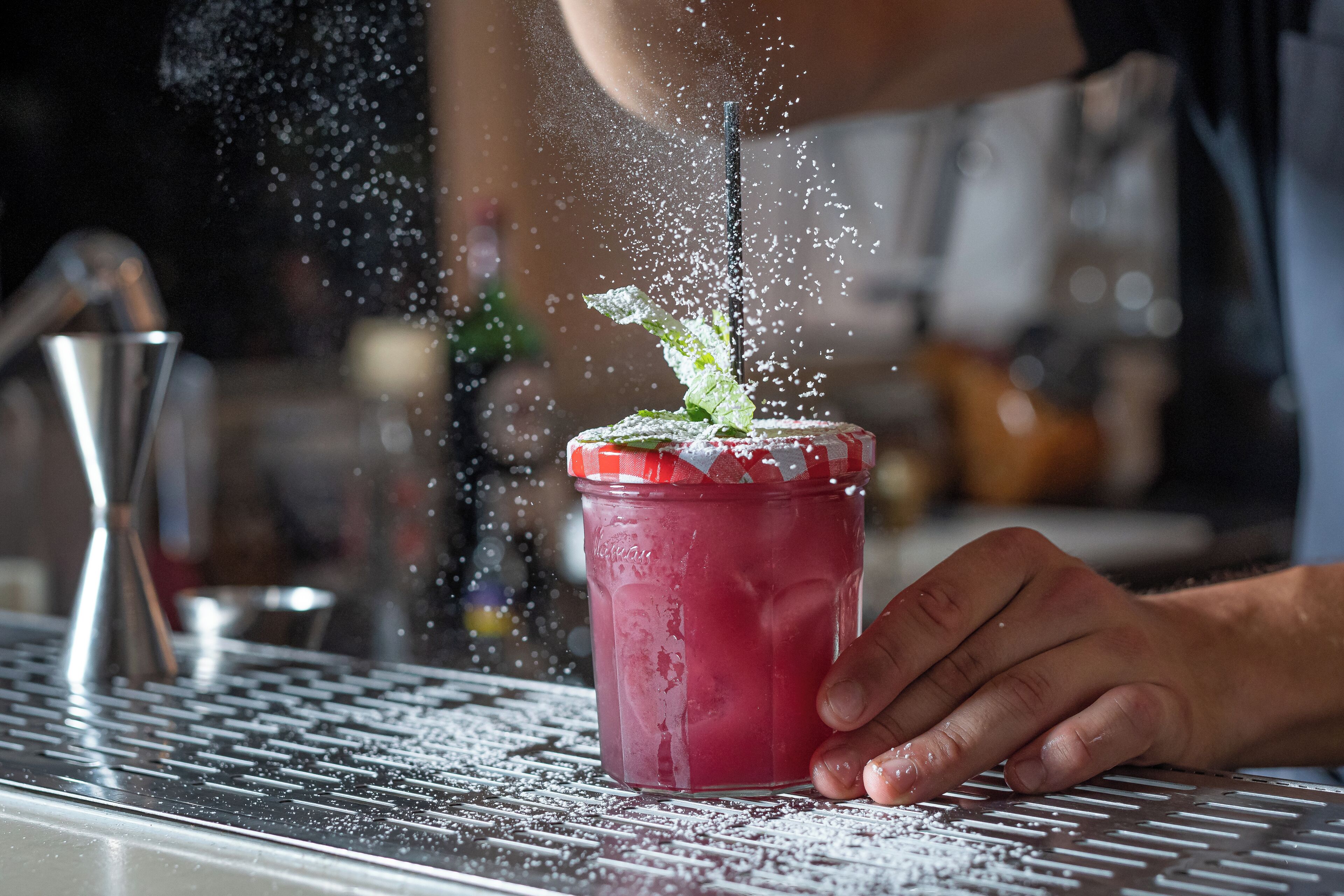 A hand holding a jar with a straw, with a liquid being poured into it.