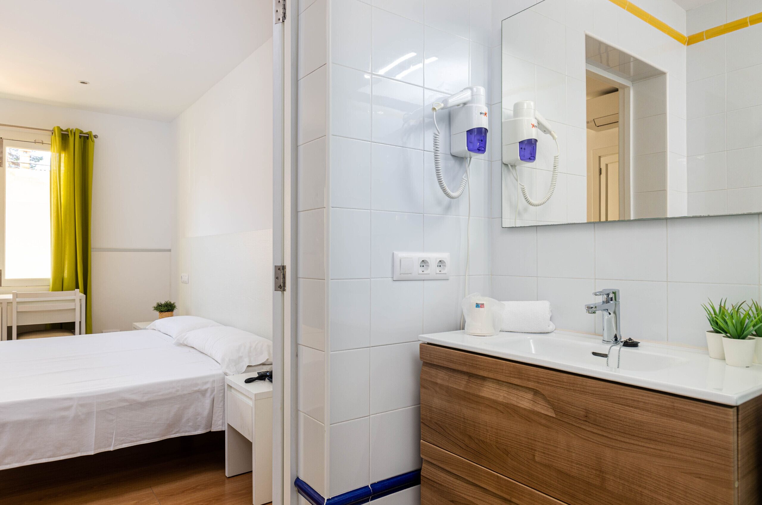 Een hotelkamer met een bed, een houten kaptafel met een wastafel en een föhn aan de muur.