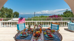 A table set with fruits, drinks, and a bottle, overlooking a scenic view. - Villa Vavilla in Paxi (Paxos)