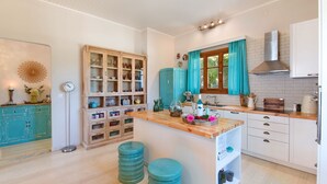 A modern kitchen with a central island, wooden cabinets, and a teal color scheme. - Villa Vavilla in Paxi (Paxos)