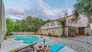 A poolside area with lounge chairs, a stone pool, and a stone wall with a balcony. - Villa Vavilla in Paxi (Paxos)