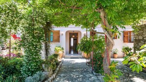 A stone pathway leading to a white building with wooden shutters and a door. - Villa Vavilla in Paxi (Paxos)