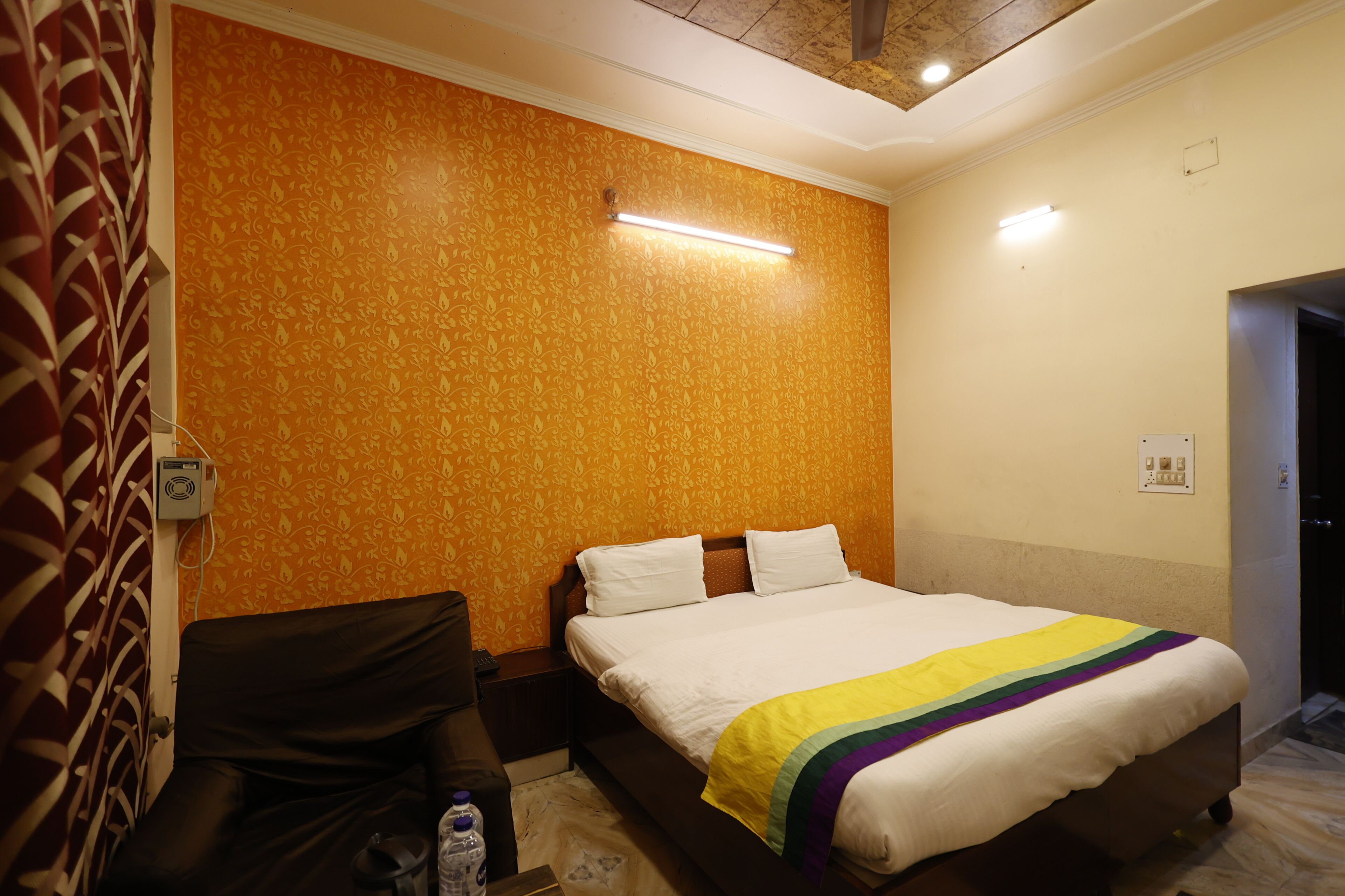 A hotel room with a bed, a nightstand, a chair, and a wall with a patterned wallpaper.