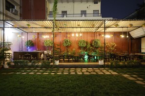 An outdoor seating area with tables and chairs, potted plants, and a sign reading 'kameshut.' - Hotel Kameshut Garden Bar and Restaurant (Varanasi)
