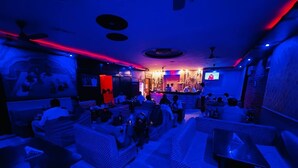 Un espace bar à la lumière tamisée, avec des canapés et des tables, un comptoir et un écran de télévision.