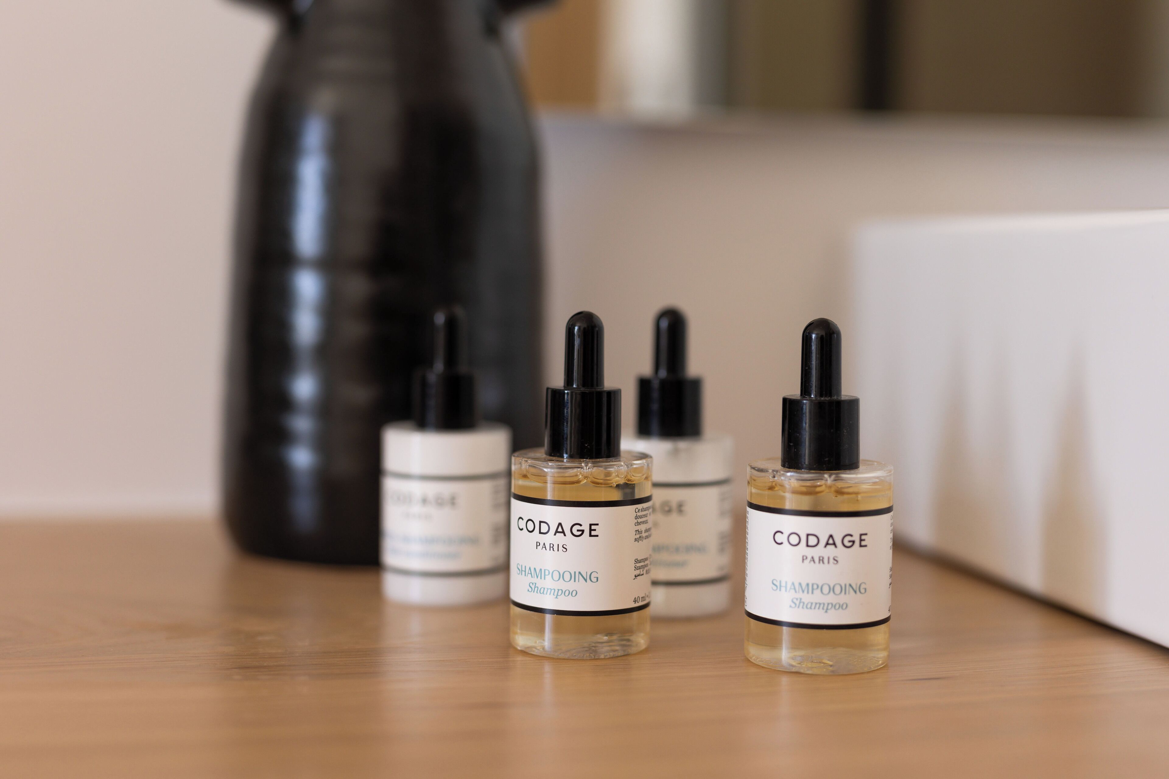 Three bottles of CODAGE Paris shampooing shampoo on a wooden surface with a black vase in the background.