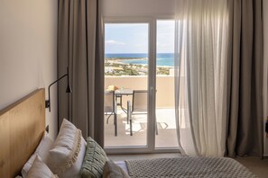 Un dormitorio con una cama grande, vistas a la playa y un balcón con mesa y sillas.