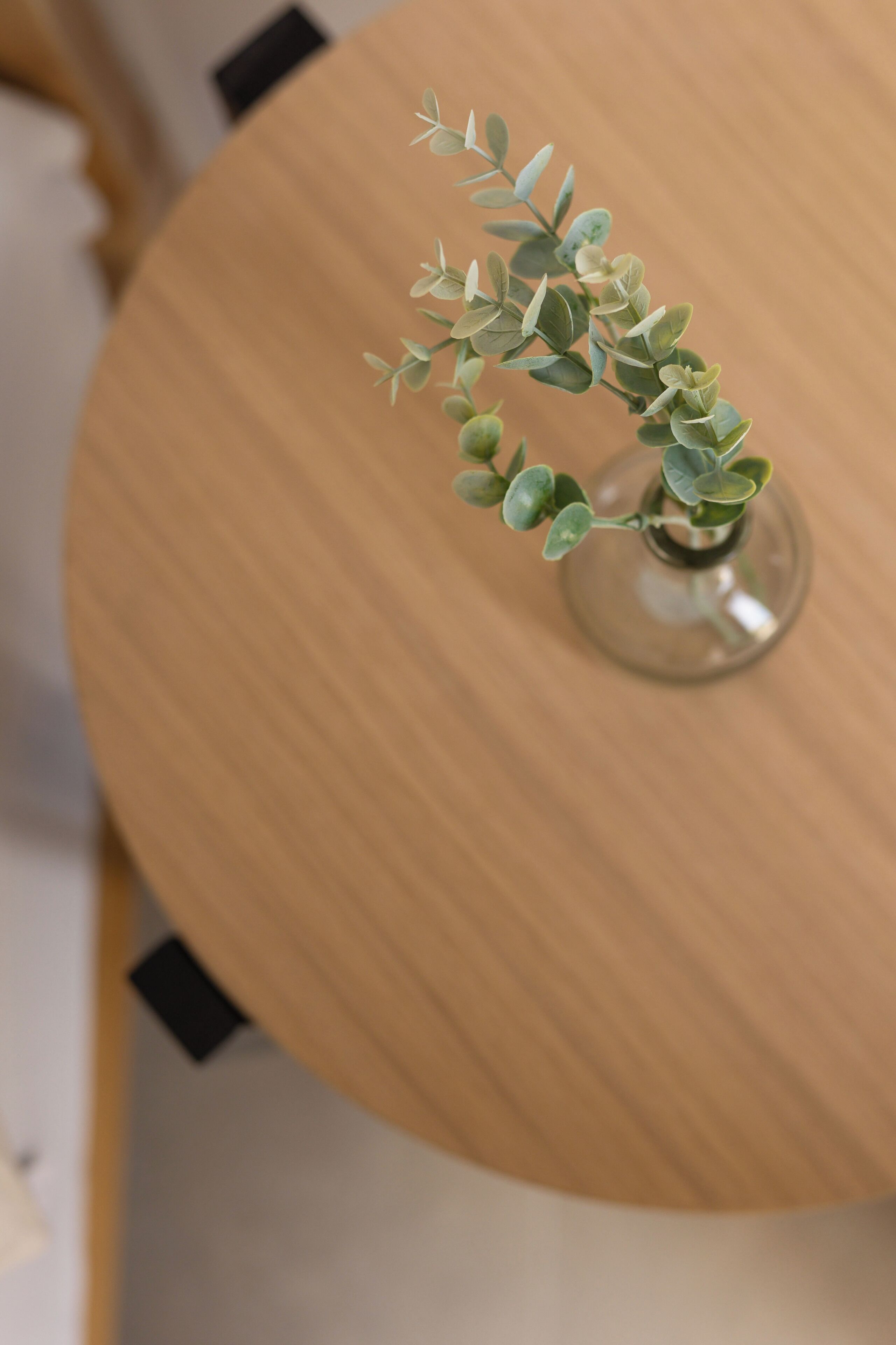 A round wooden table with a clear glass vase containing a small plant with green leaves.