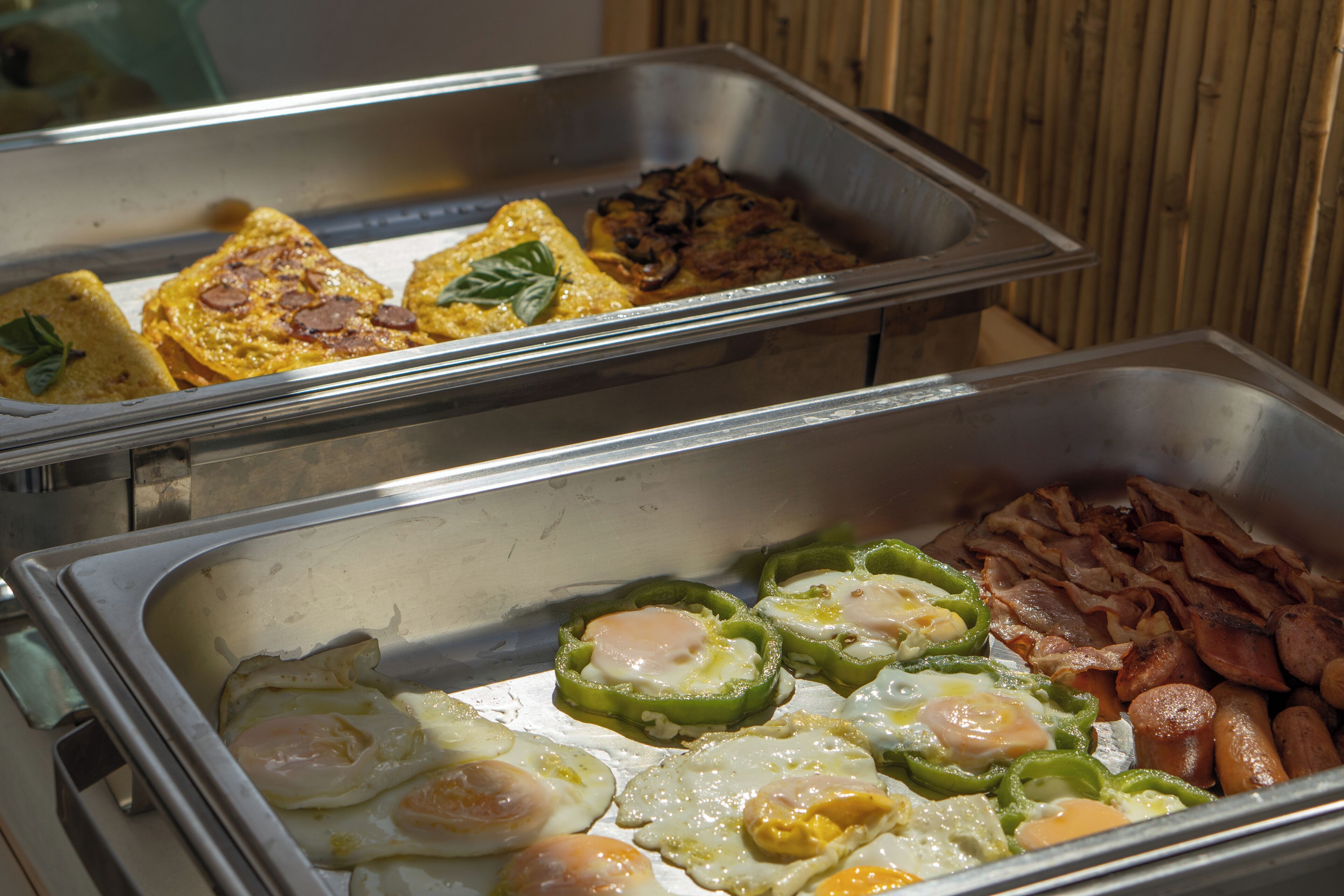 Un bufé con diversos alimentos para el desayuno, como huevos, tocino y tortillas.